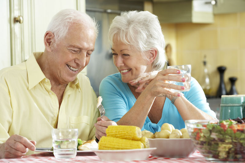 a picture of an older couple smiling at each other over the dinner table because they have improved their smile with implant supported dentures.