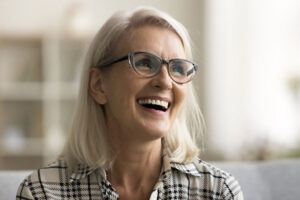 Smiling senior woman with glasses looking joyful, showing confidence and happiness after receiving dental implants.